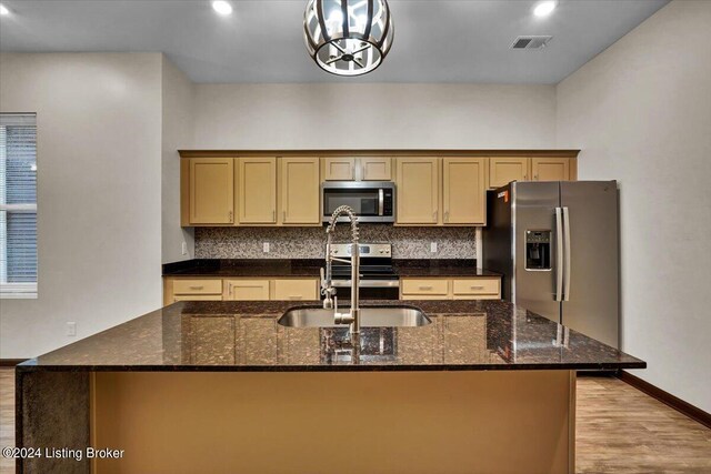 kitchen with light hardwood / wood-style floors, appliances with stainless steel finishes, a center island with sink, and tasteful backsplash