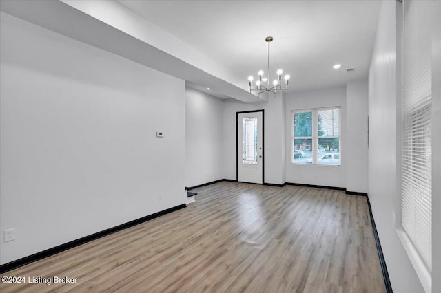 empty room with light hardwood / wood-style flooring and a notable chandelier