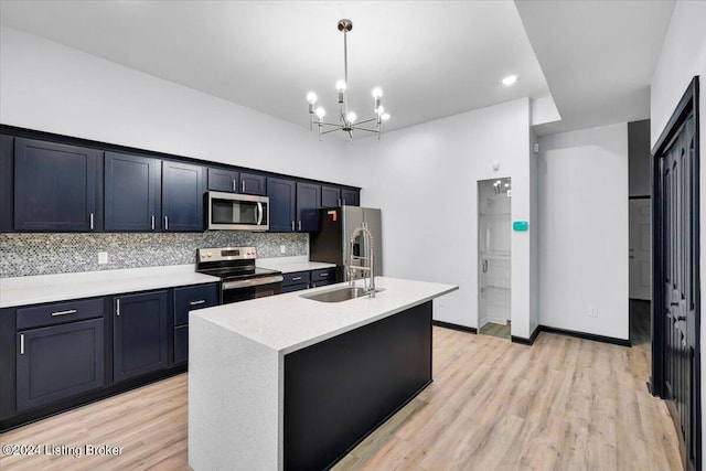 kitchen with light wood-type flooring, a kitchen island with sink, tasteful backsplash, stainless steel appliances, and an inviting chandelier