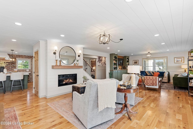 living room with brick wall, light wood-type flooring, a chandelier, and a fireplace