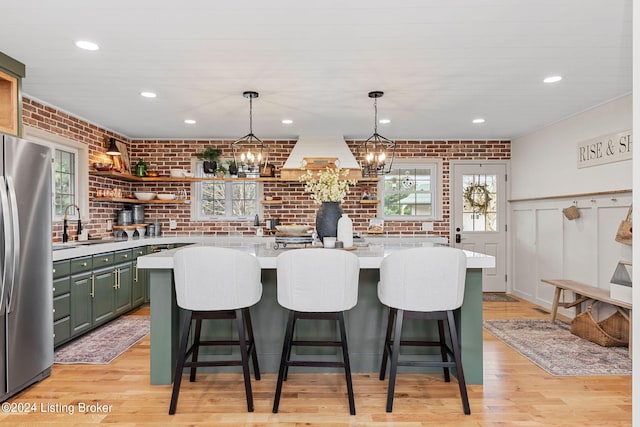 kitchen with brick wall, light hardwood / wood-style flooring, a center island, stainless steel refrigerator, and a wealth of natural light