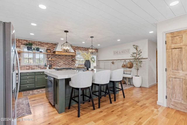 kitchen featuring brick wall, a kitchen island, stainless steel fridge, light hardwood / wood-style flooring, and a kitchen bar