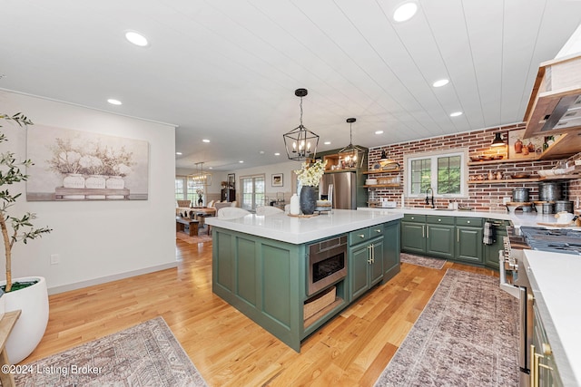 kitchen with green cabinets, light hardwood / wood-style flooring, appliances with stainless steel finishes, brick wall, and a kitchen island