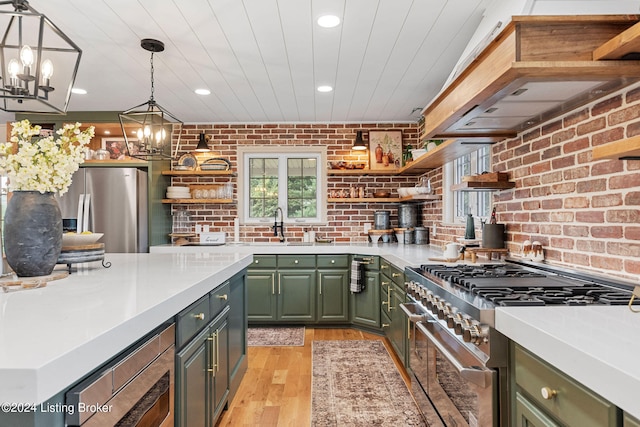 kitchen featuring light wood-type flooring, a chandelier, stainless steel appliances, decorative light fixtures, and brick wall