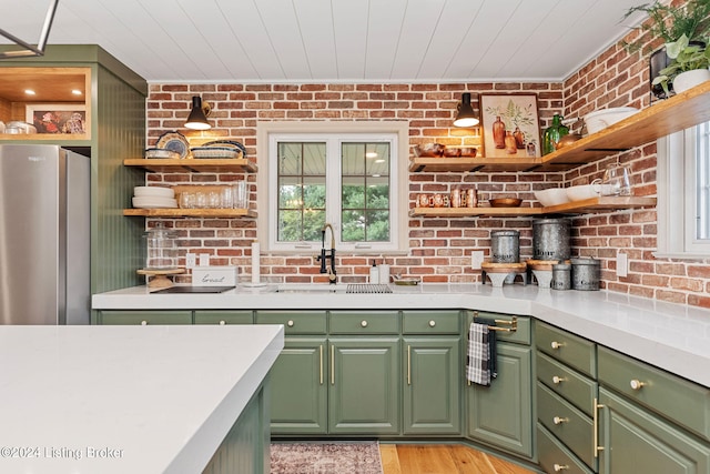 kitchen featuring green cabinetry, sink, stainless steel refrigerator, and brick wall