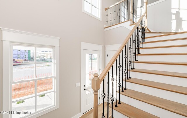 stairway with a towering ceiling, hardwood / wood-style flooring, and a healthy amount of sunlight