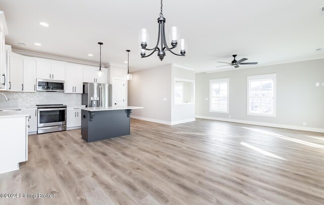 kitchen featuring ceiling fan with notable chandelier, backsplash, appliances with stainless steel finishes, a center island, and light wood-type flooring