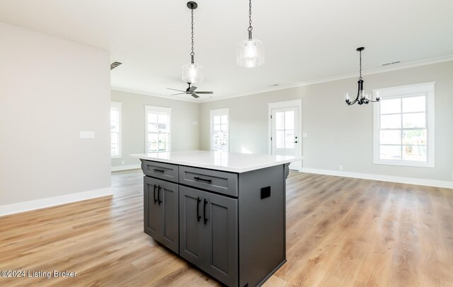 kitchen featuring a kitchen island, ceiling fan with notable chandelier, hanging light fixtures, ornamental molding, and light wood-type flooring