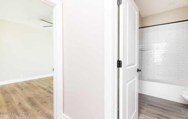 bathroom with wood-type flooring, toilet, tiled shower / bath, and ceiling fan