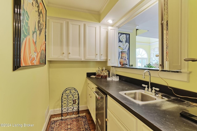 kitchen with a sink, white cabinetry, ornamental molding, stainless steel dishwasher, and dark countertops