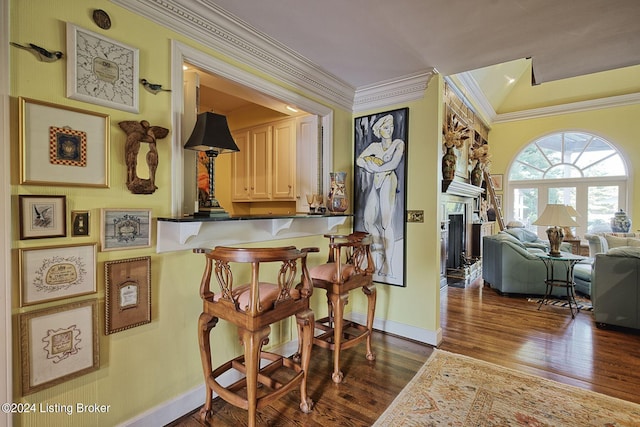 kitchen featuring crown molding, a fireplace, a kitchen bar, dark wood finished floors, and baseboards
