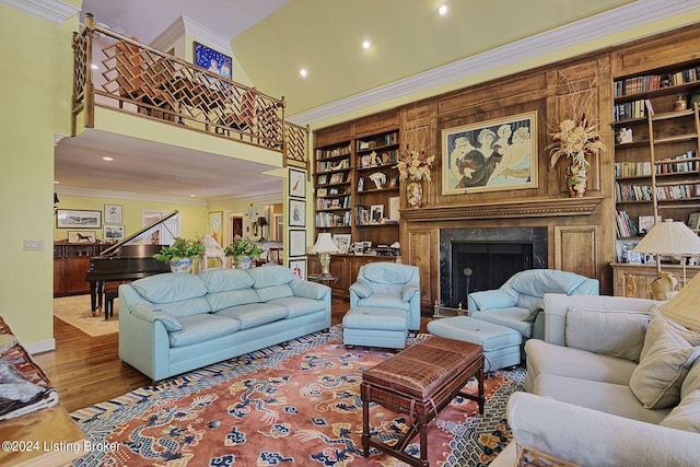 living area with built in features, crown molding, a high ceiling, a high end fireplace, and wood finished floors