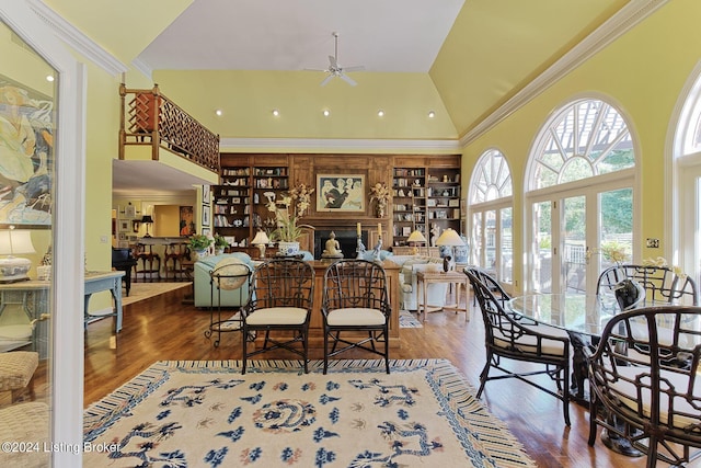 dining area with high vaulted ceiling, a fireplace, wood finished floors, a ceiling fan, and ornamental molding