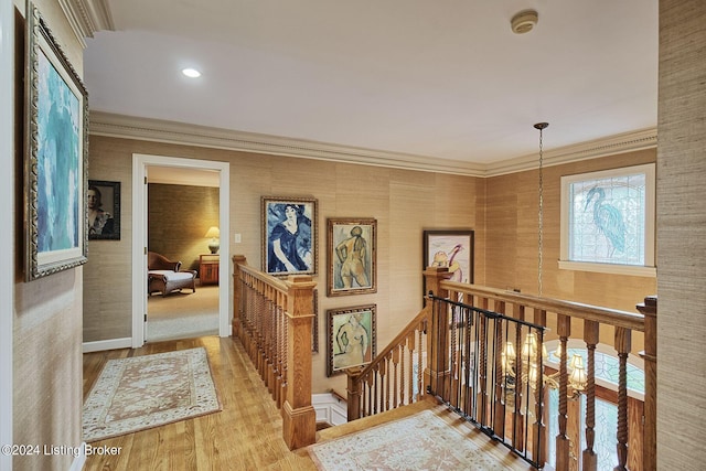 hall with wood finished floors, an upstairs landing, and ornamental molding