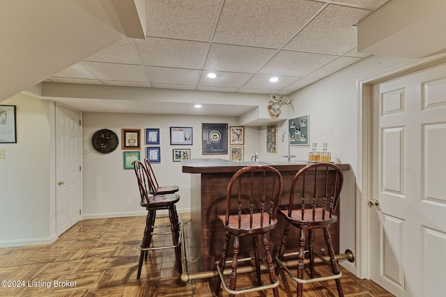 bar with baseboards, indoor wet bar, a paneled ceiling, and recessed lighting