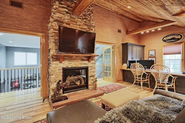 living room with visible vents, wood finished floors, a stone fireplace, high vaulted ceiling, and beam ceiling