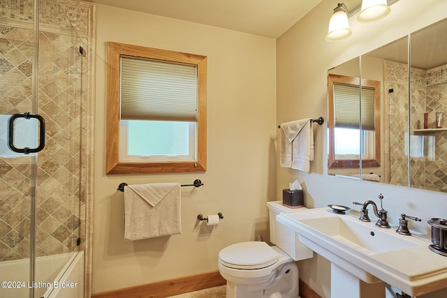 bathroom with toilet, a sink, a shower with door, and baseboards