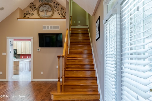 staircase featuring high vaulted ceiling and hardwood / wood-style flooring