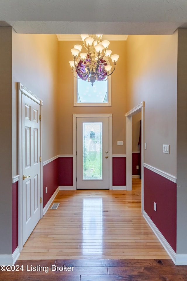 entrance foyer with crown molding, an inviting chandelier, and light hardwood / wood-style floors