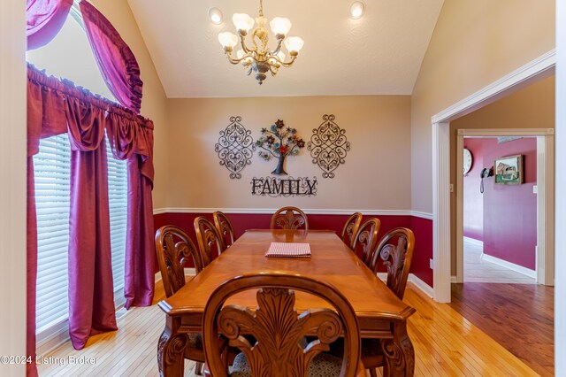 dining space with light wood-type flooring, a notable chandelier, and vaulted ceiling