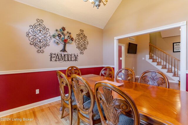 dining space with lofted ceiling, light wood-type flooring, and a notable chandelier