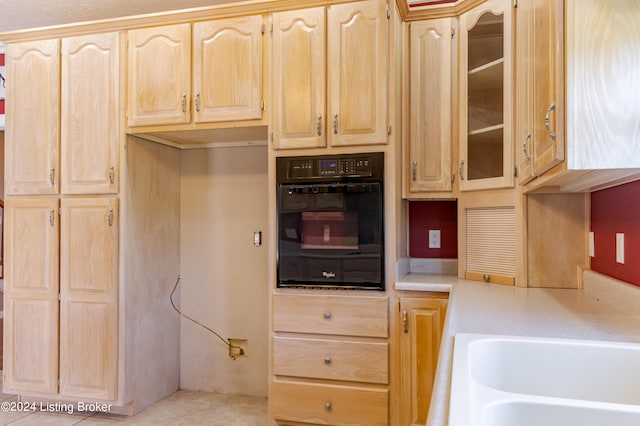 kitchen with light brown cabinetry, black oven, and light tile patterned flooring