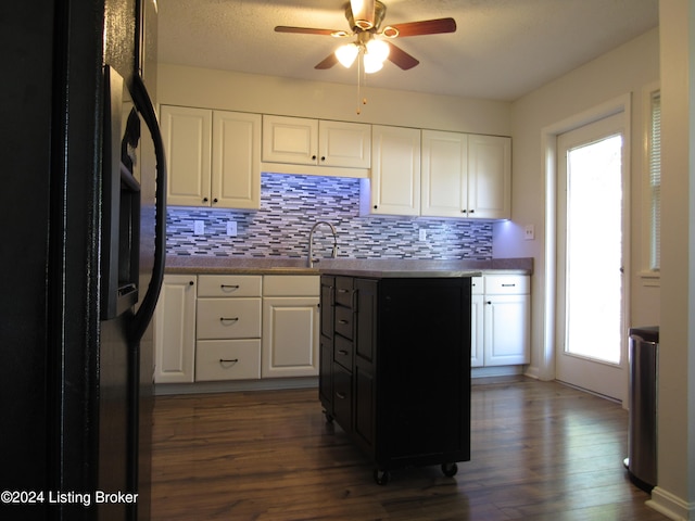 kitchen with black fridge, dark wood-type flooring, tasteful backsplash, and white cabinetry