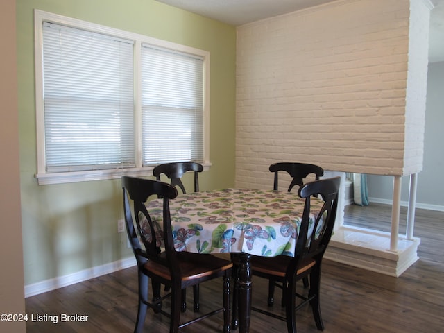 dining area with dark hardwood / wood-style flooring and brick wall