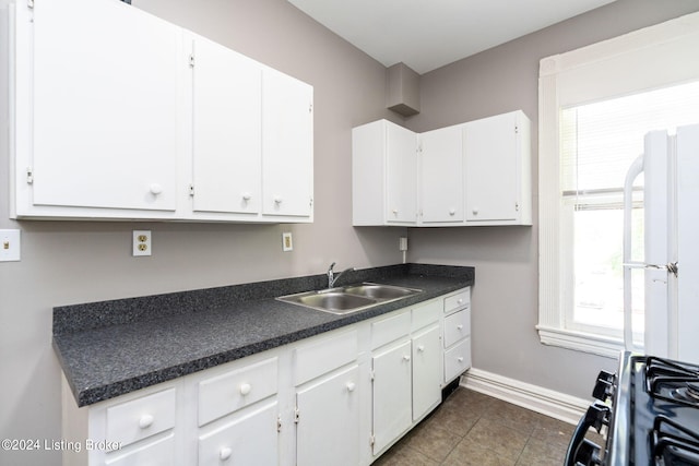 kitchen with white cabinets, dark tile patterned flooring, sink, and range