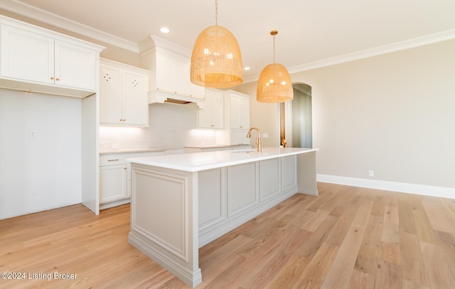 kitchen featuring a kitchen island with sink, light wood-type flooring, white cabinets, and hanging light fixtures