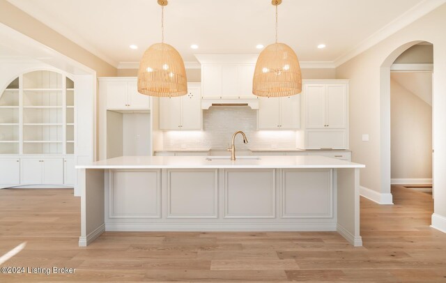 kitchen featuring decorative light fixtures, light wood-type flooring, and an island with sink