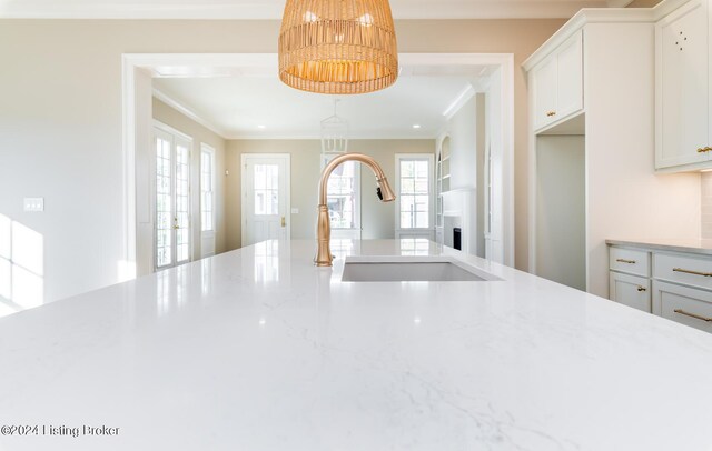 kitchen with a fireplace, light stone countertops, white cabinetry, sink, and ornamental molding