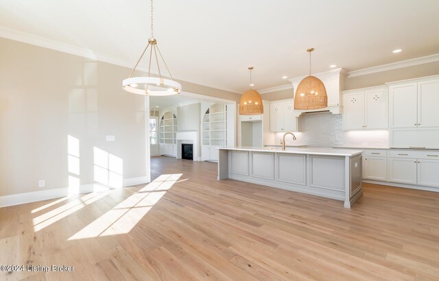 kitchen with a kitchen island with sink, pendant lighting, white cabinetry, and light hardwood / wood-style floors