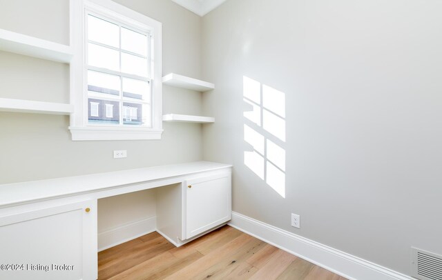 unfurnished office featuring built in desk and light hardwood / wood-style floors