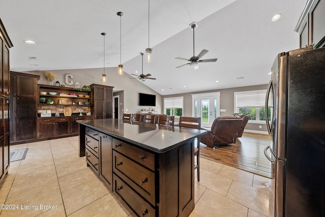 kitchen with open floor plan, a kitchen bar, freestanding refrigerator, and dark brown cabinetry