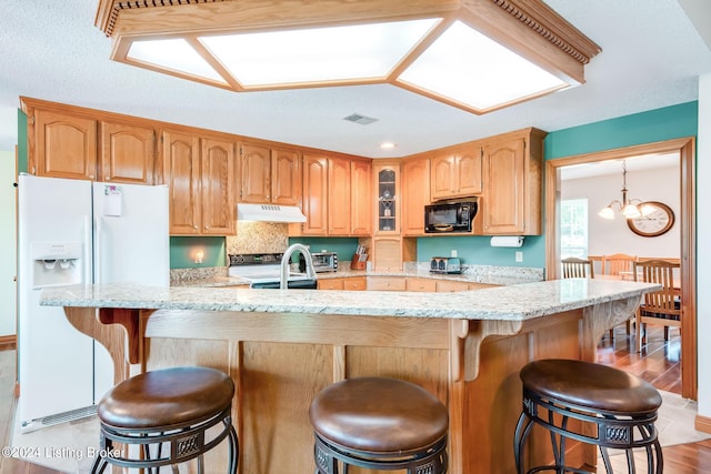 kitchen featuring stainless steel electric range oven, light hardwood / wood-style flooring, light stone counters, white refrigerator with ice dispenser, and a breakfast bar area