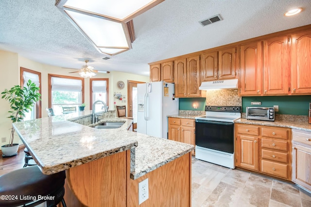 kitchen featuring white appliances, an island with sink, sink, ceiling fan, and light stone counters