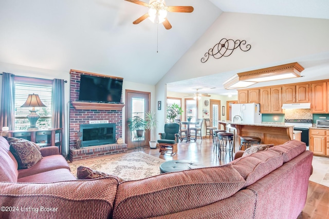 living room featuring light wood-type flooring, ceiling fan, a wealth of natural light, and a fireplace