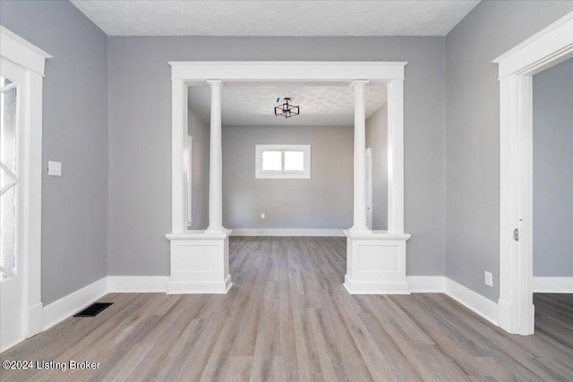 unfurnished living room featuring ornate columns, a textured ceiling, and light hardwood / wood-style floors