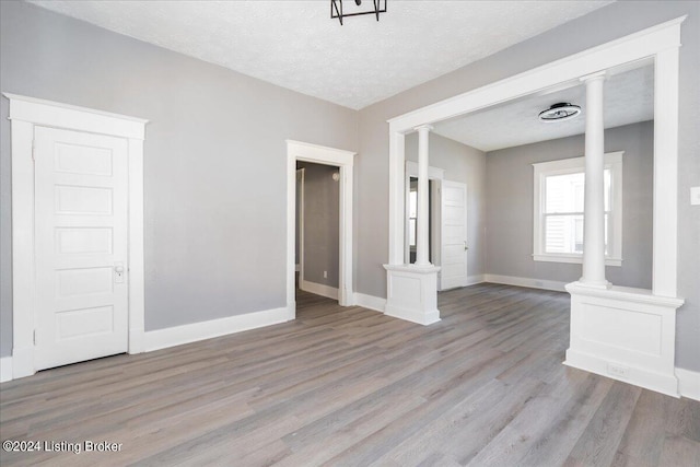 unfurnished living room featuring ornate columns, light hardwood / wood-style floors, and a textured ceiling