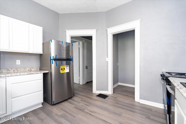 kitchen with stainless steel fridge, electric range, white cabinetry, a textured ceiling, and light hardwood / wood-style floors