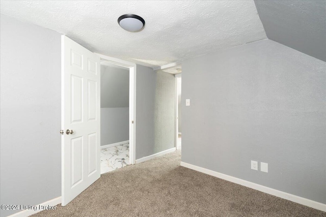 unfurnished room with a textured ceiling, vaulted ceiling, and carpet flooring