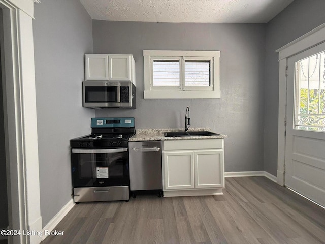 kitchen with hardwood / wood-style flooring, stainless steel appliances, sink, white cabinets, and a textured ceiling