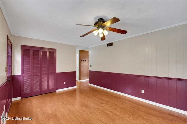 unfurnished room featuring wooden walls, crown molding, a textured ceiling, light hardwood / wood-style flooring, and ceiling fan