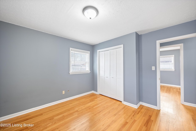 unfurnished bedroom featuring multiple windows, a textured ceiling, light hardwood / wood-style floors, and a closet