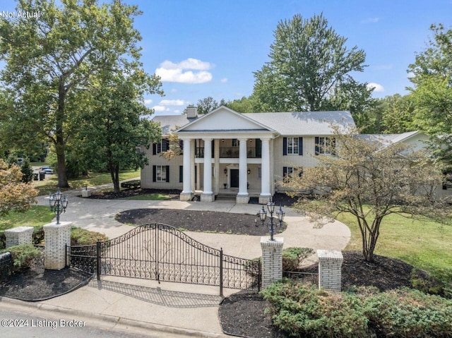 greek revival inspired property with driveway, a fenced front yard, a chimney, a gate, and a porch