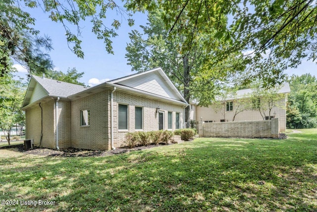 view of side of property with brick siding, a yard, and fence