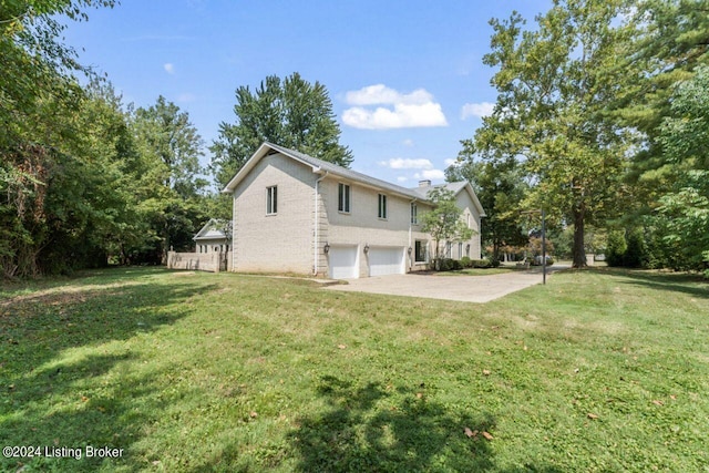 view of side of home featuring an attached garage, driveway, a chimney, and a lawn