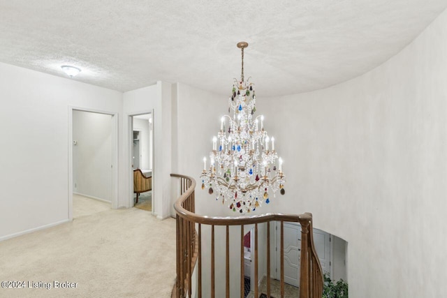 hall featuring a chandelier, a textured ceiling, an upstairs landing, baseboards, and carpet