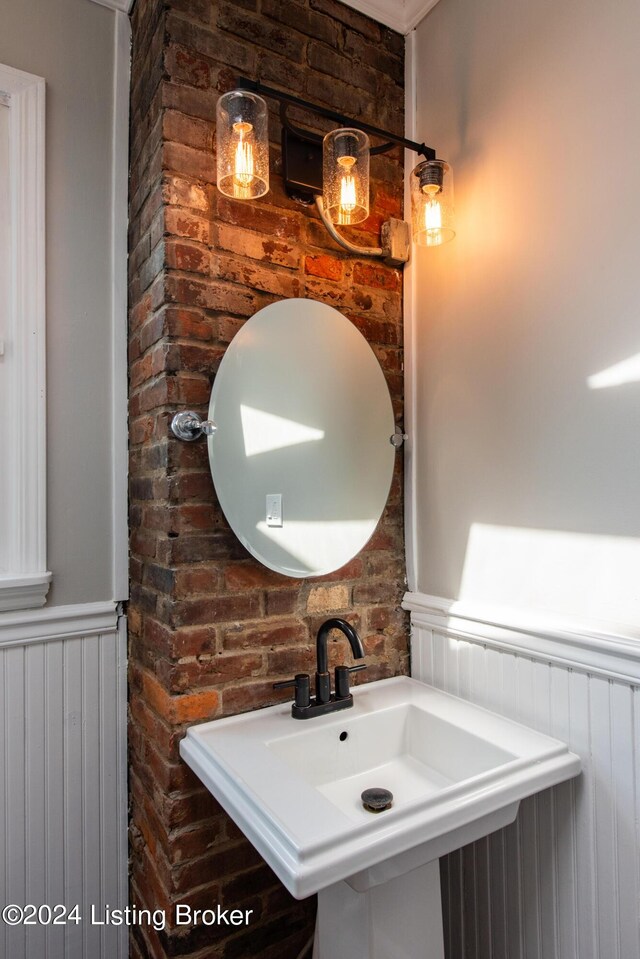 bathroom with brick wall, wainscoting, and a sink